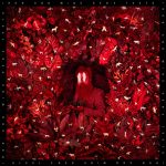 Hen's Teeth album cover. The artist is in the middle of a grove of leaves, surrounded by small white paper animals. There are two white feathers over his eyes, and he is holding a bunch of grapes. Everything is coloured red.